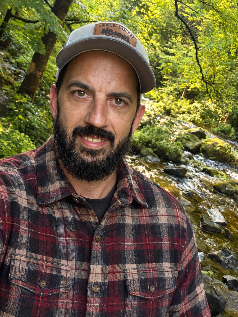 The maker of Lake Woodcraft, smiling, standing by a creek in the woods