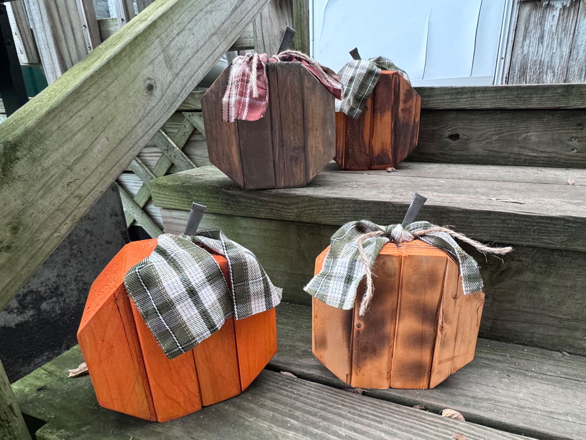 Three handmade wooden pumpkins with plaid fabric ribbons on a set of wooden steps