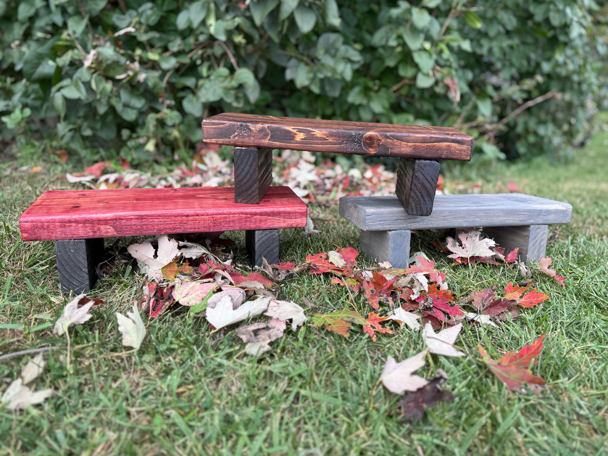 Three handmade wooden risers finished in red, gray, and dark stain, sitting on grass